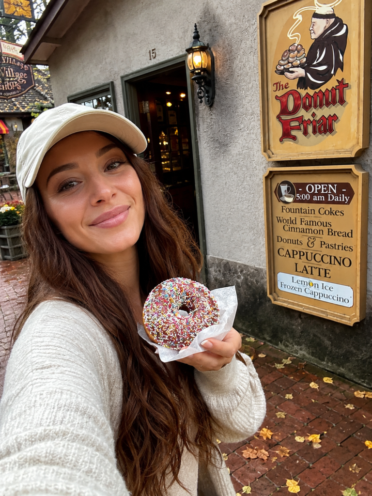 Woman holding a sprinkled donut outside The Donut Friar in Gatlinburg’s Village Shops on a cool Smoky Mountain morning.