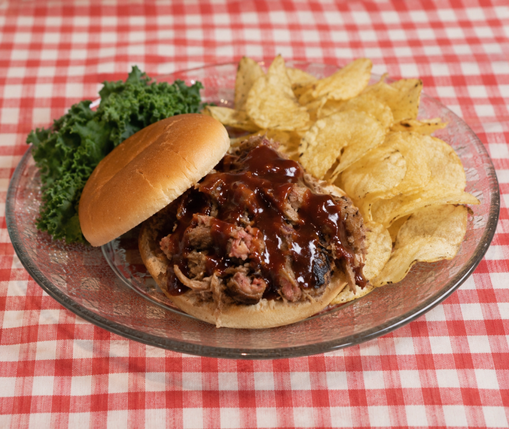 Pulled pork BBQ sandwich with potato chips on a glass plate at a Smoky Mountain restaurant in Gatlinburg.