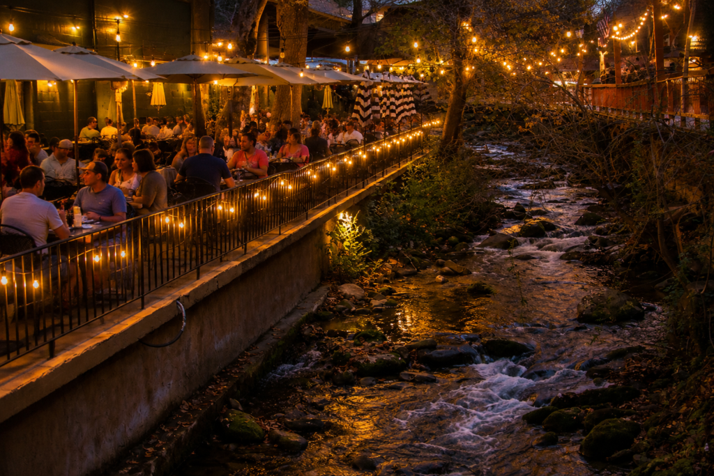 Best Dinner Restaurants in Gatlinburg: Smoky Mountain Favorites Worth the Wait 2 Crowded creekside restaurant patio in Gatlinburg at night with glowing string lights and Smoky Mountain evening atmosphere