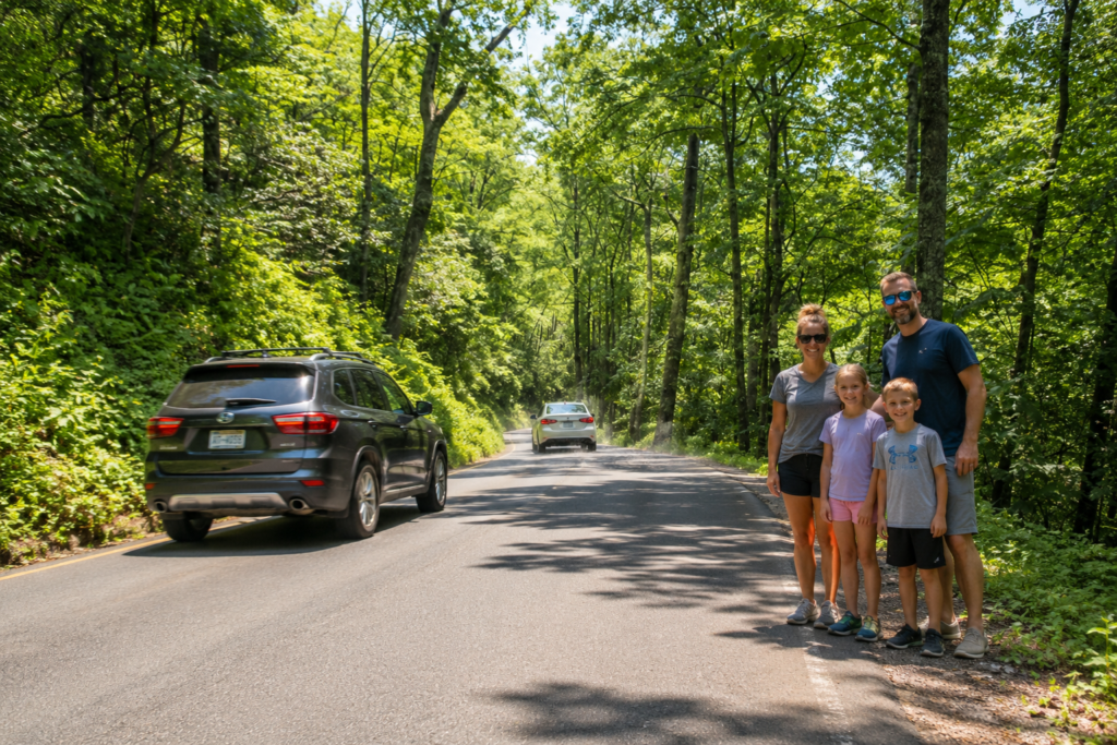 Family standing beside Ski Mountain Road in Gatlinburg during summer with cars driving through the Smoky Mountains