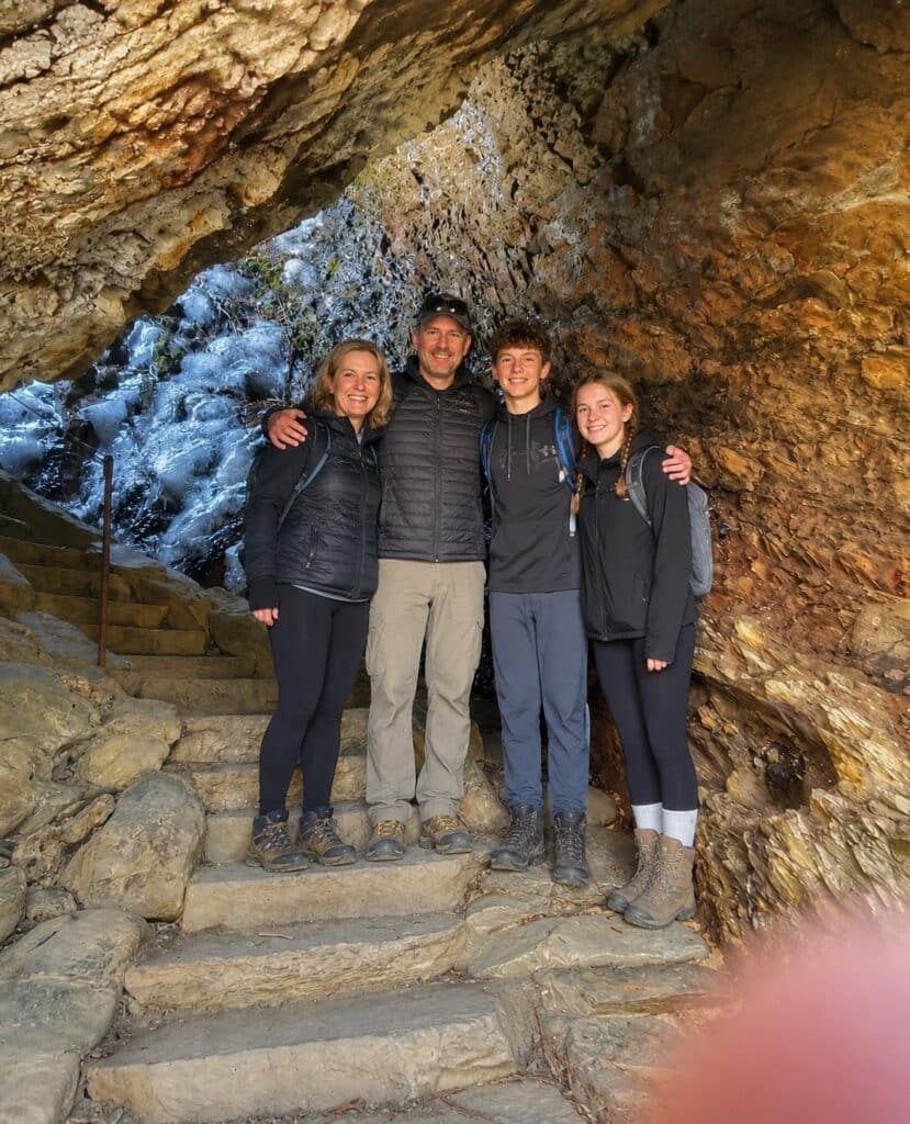 A smiling family of four poses on the stone steps inside Alum Cave along the Alum Cave Trail in Great Smoky Mountains National Park. One of many of the best hiking trails in the Great Smoky Mountains