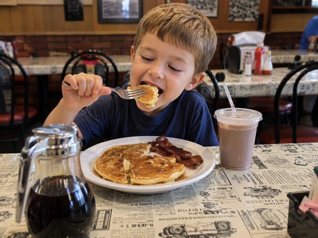 Child eating pancakes and bacon with chocolate milk during breakfast in Gatlinburg