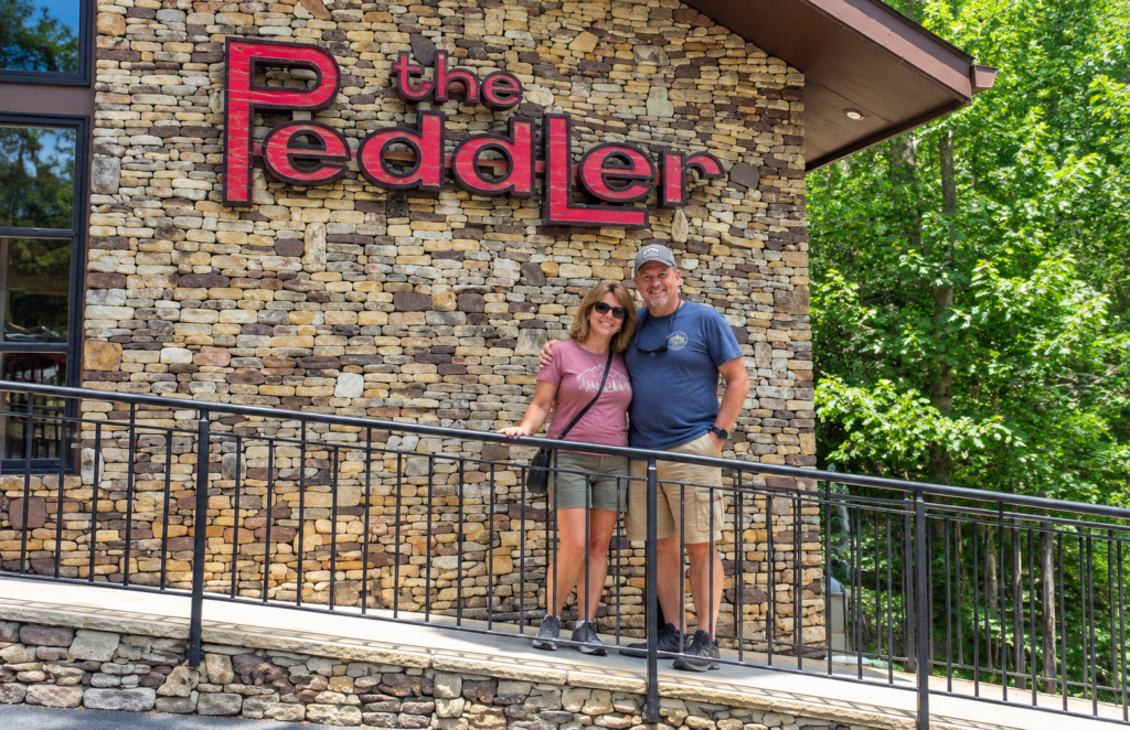 Middle-aged couple posing beneath The Peddler Steakhouse sign in Gatlinburg